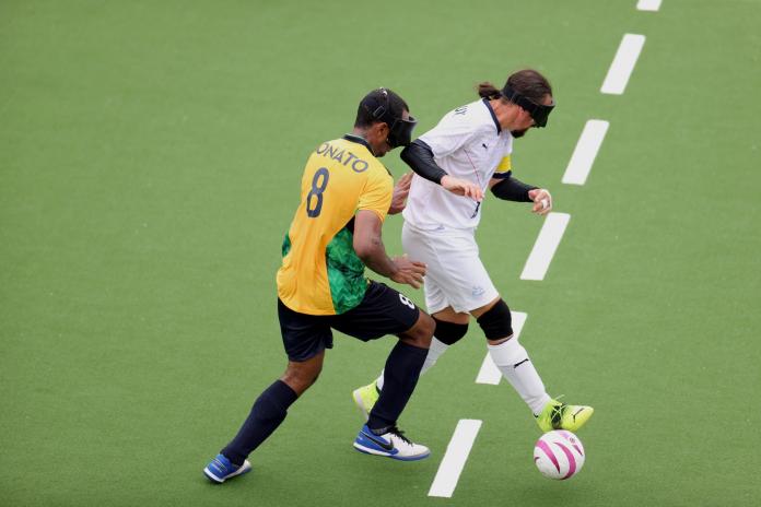 A male blind football player dribbles the ball past an opponent.