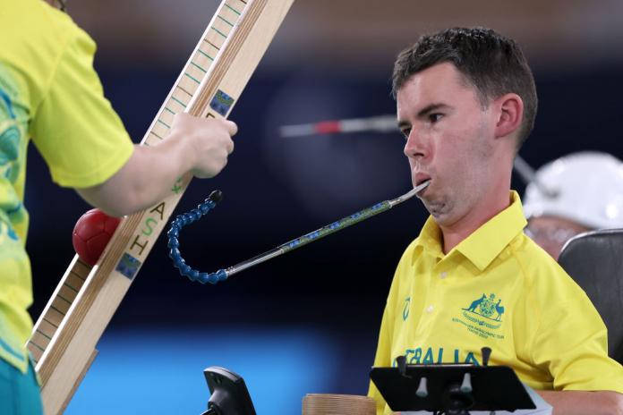 Australian boccia athlete Daniel Michel controls an equipment in his mouth to roll the boccia ball on a ramp.